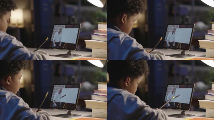 后视图，9岁男孩的非裔美国人在平板电脑上通过视频通话与导师老师在家上学时，晚上呆在家里。家庭教育和远