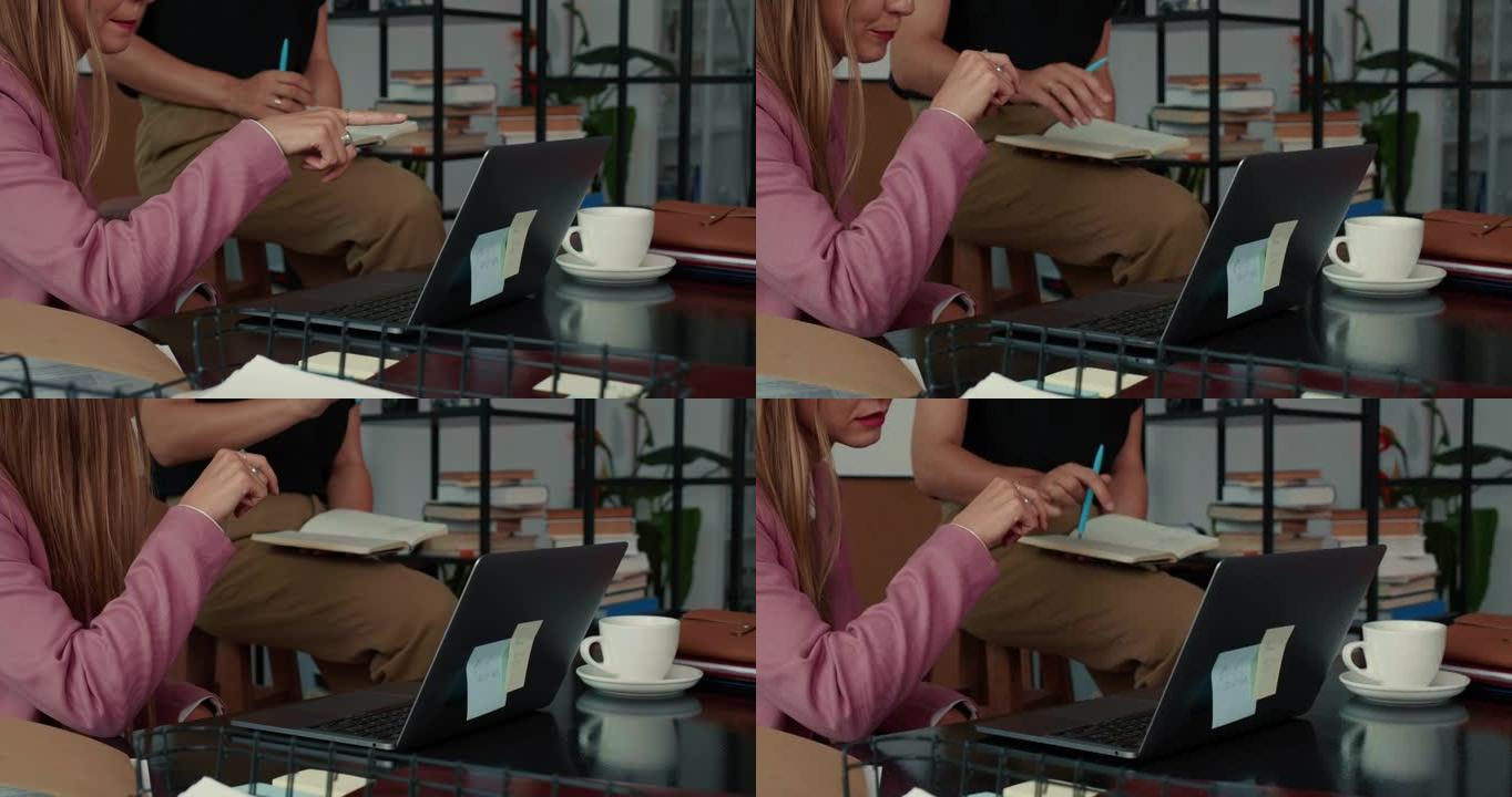 合作理念。两个快乐美丽忙碌的年轻商务女性在现代办公桌上用笔记本电脑微笑。