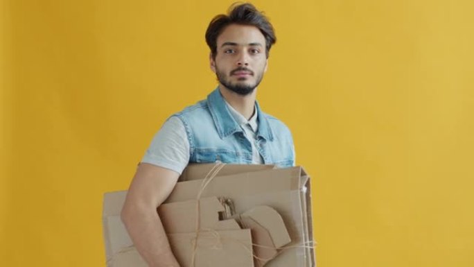 中东家伙的肖像在黄色背景上携带纸板进行回收