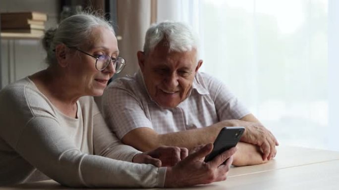 微笑的已婚夫妇在智能手机屏幕上观看视频