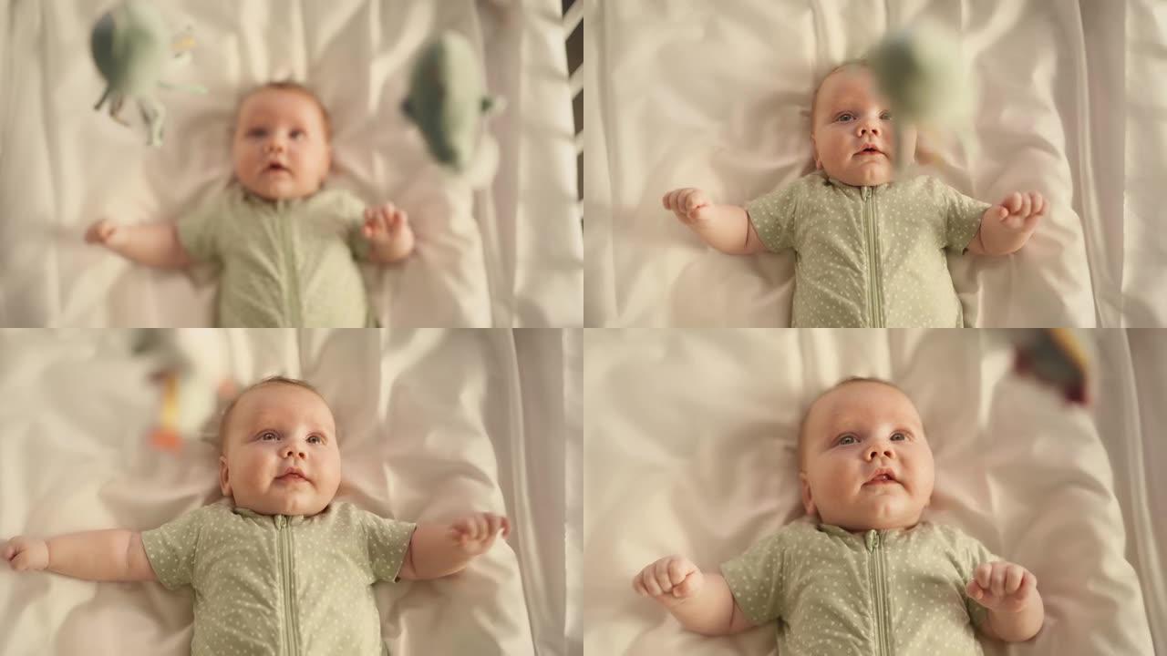 一个可爱的新生婴儿躺在婴儿床背上的转移焦点镜头。一个兴奋的幼儿看着旋转的玩具的嬉戏肖像。童年、新生活
