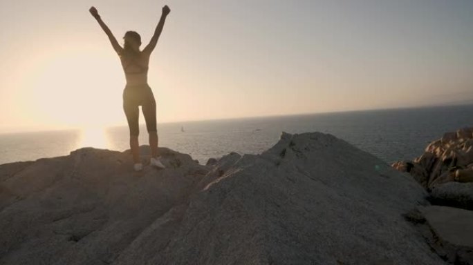 一位年轻的运动运动运动员，身体结实，对自己的成就感到满意，因为她在日落时在带有海景的岩石上跑步和慢跑