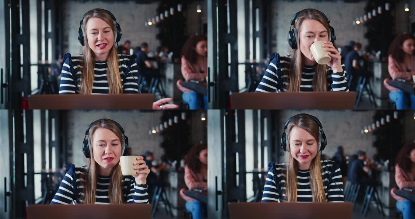 年轻快乐微笑的女性金发信息技术自由工作者使用笔记本电脑，耳机在时尚咖啡馆在线与朋友聊天