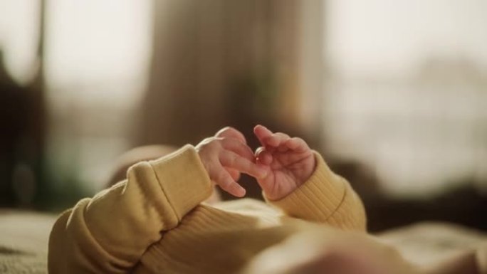 黄色套头衫中一个可爱的婴儿的手的特写镜头。试图交流和咕咕的活跃的小孩。小手掌准备发现新世界并接受爱