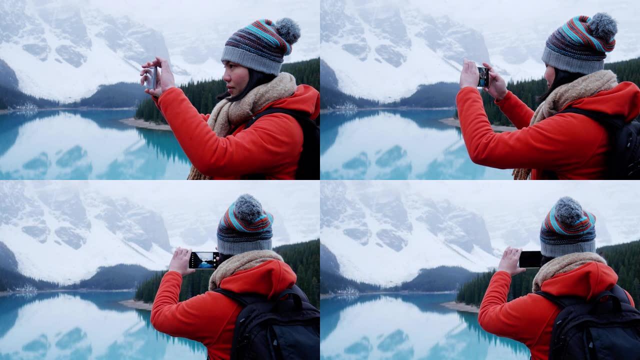 女旅行者在加拿大艾伯塔省的冰碛湖班夫用智能手机拍照