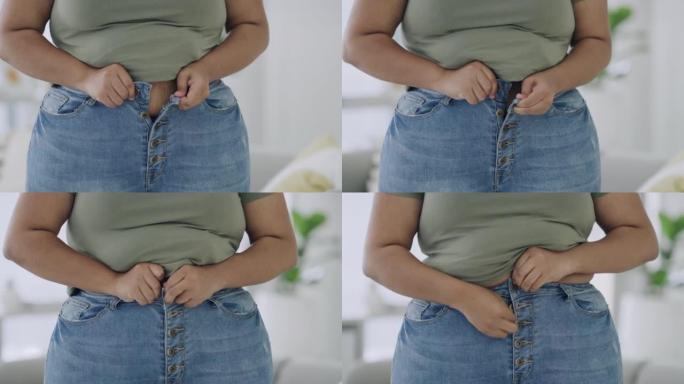 一个稍微超重的女性在家里的房间里努力穿上她的牛仔裤子的特写镜头。女人的裤子不合身，因为她的腰部和臀部