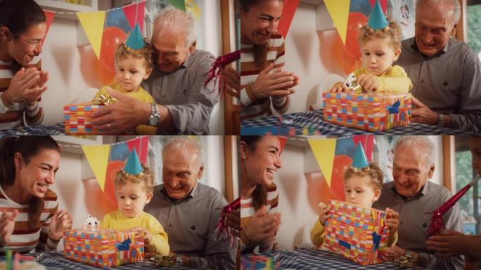 一个快乐的家庭为一个可爱的小男孩庆祝生日的肖像:爷爷给他的孙子一个包装好的礼物，而其他的家庭成员在鼓