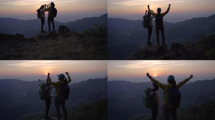 两个女人徒步上山，在山顶上击掌，举手庆祝成功