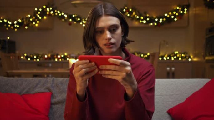 一位穿着红色毛衣的美丽棕色头发的女人在她的红色智能手机上向重要人物打了一条消息，坐在舒适的圣诞节装饰