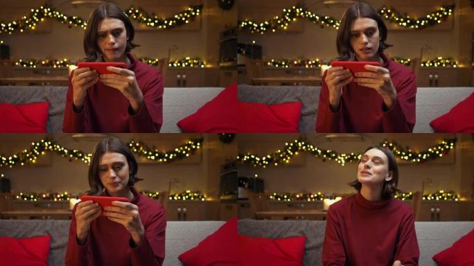 一位穿着红色毛衣的美丽棕色头发的女人在她的红色智能手机上向重要人物打了一条消息，坐在舒适的圣诞节装饰