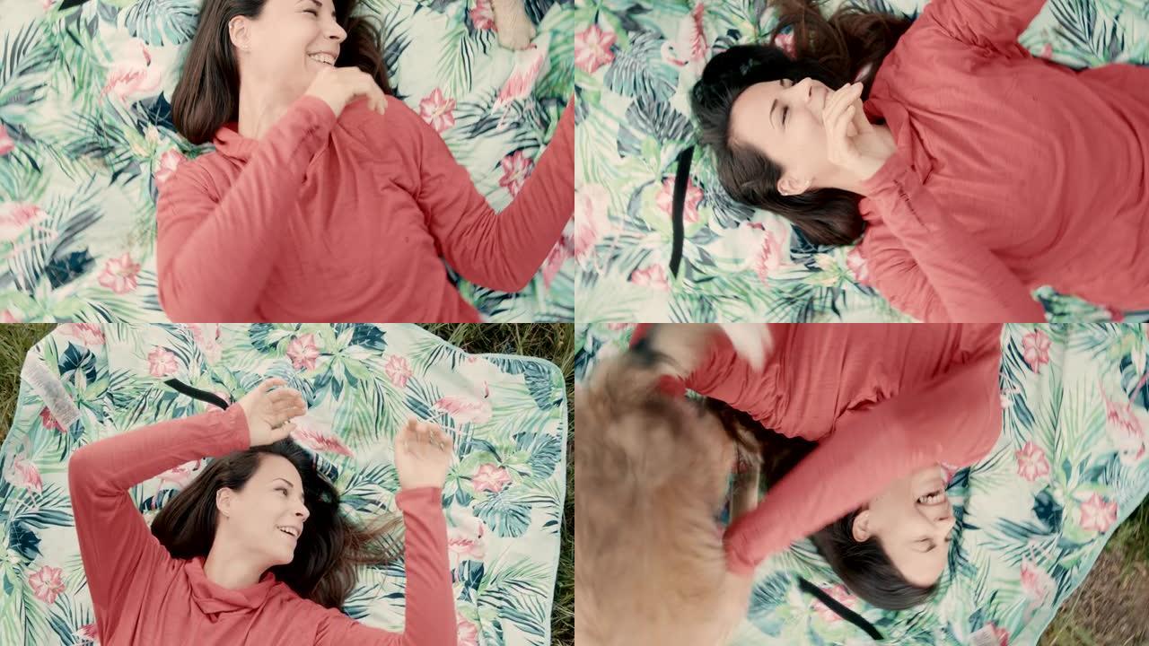 可爱的小狗和一个躺在草地上的毯子上的女人玩耍