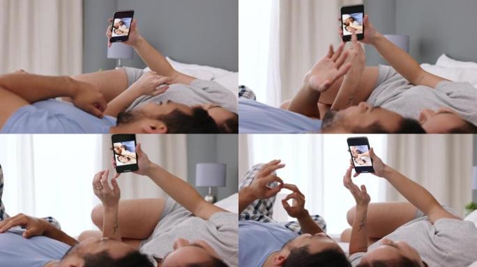 手机、自拍和社交媒体上的情侣爱分享，一起躺在卧室里穿着睡衣在家。微笑、发帖和女人和一个年轻的丈夫在网