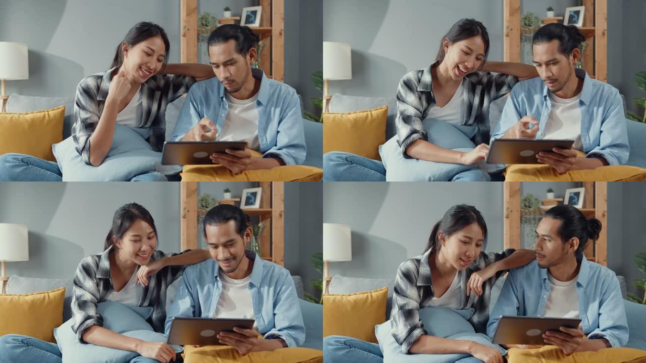 快乐的亚洲年轻迷人的夫妇坐在沙发上使用平板电脑购物在线家具装饰家在客厅在新房子。