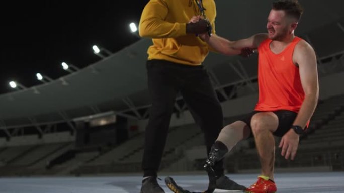 多样化的男教练帮助疲倦的残疾男运动员用奔跑的刀片站起来