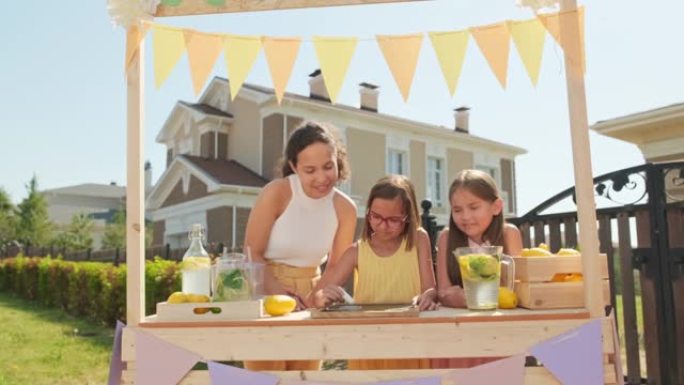 妈妈和两个在柠檬水市场有开放标志的女孩
