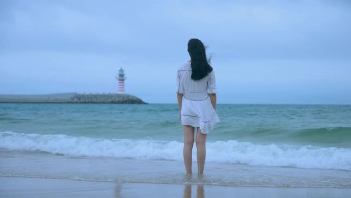 看着站在海滩上的灯塔的年轻女性