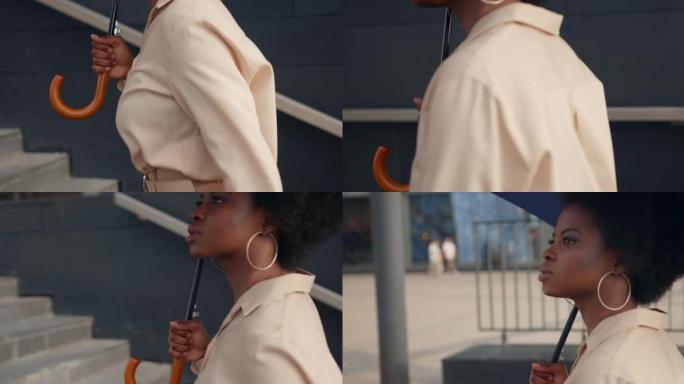一个年轻的深色皮肤的女人穿着米色衣服的耳环，蓝色的雨伞走上楼梯前往商务中心，我们一开始就看不到她的脸