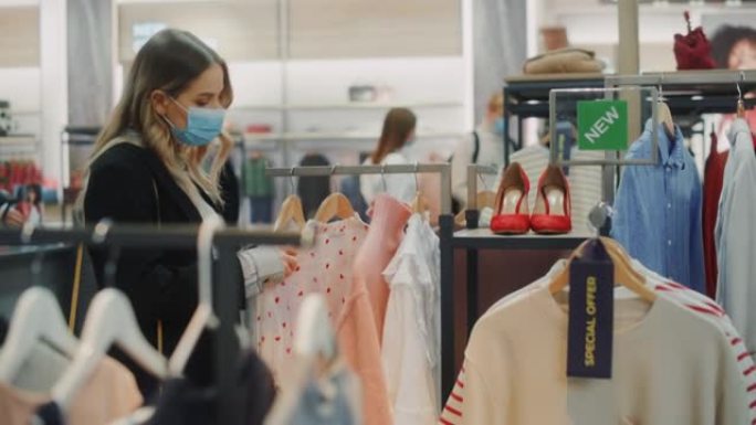 美丽的女性顾客戴着防护口罩在服装店购物。时尚零售店里的人多样化，选择时尚的服装，丰富多彩的可持续品牌