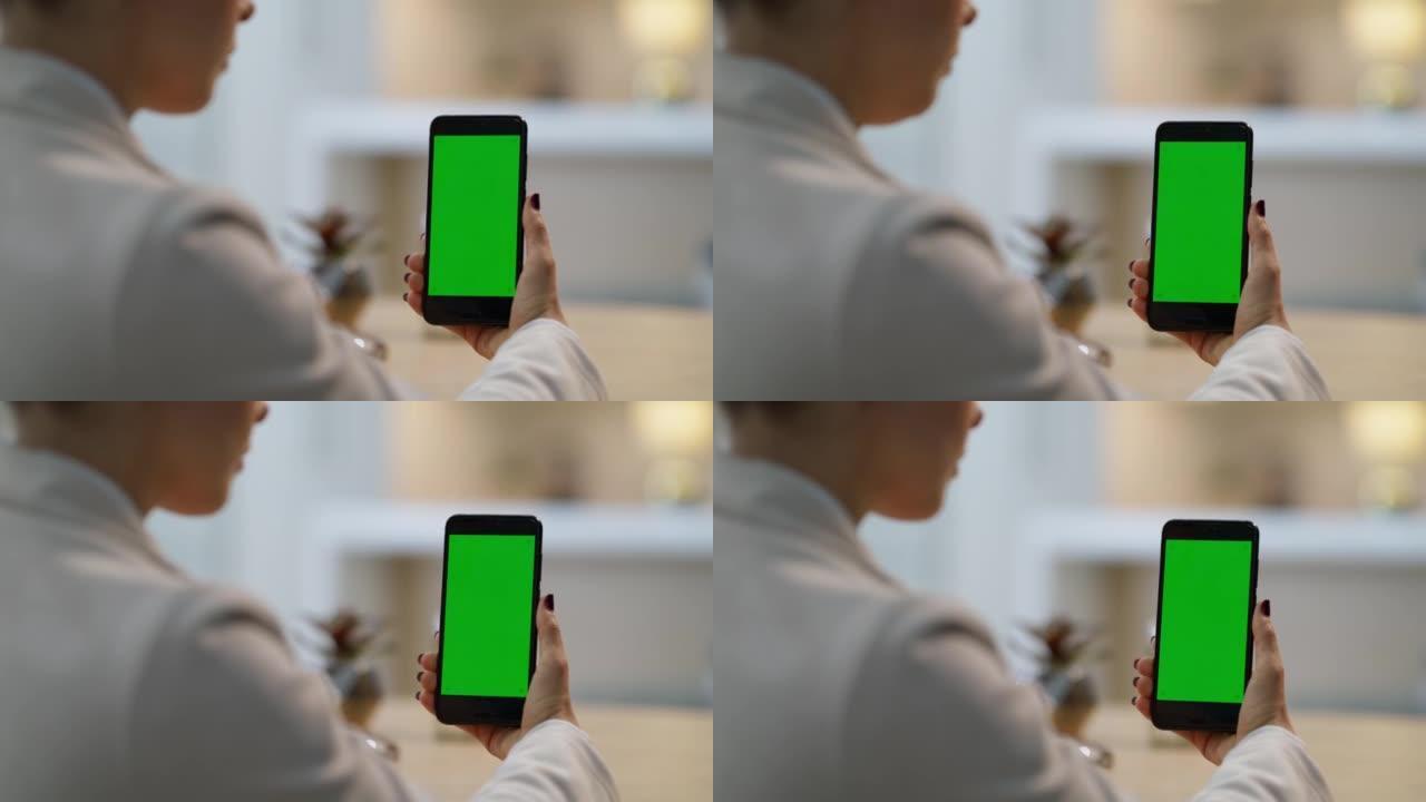 女人使用绿屏手机。女商人坐在办公桌前在办公室里拿着智能手机。在肩膀上看一位女性看着她手中的数字设备。