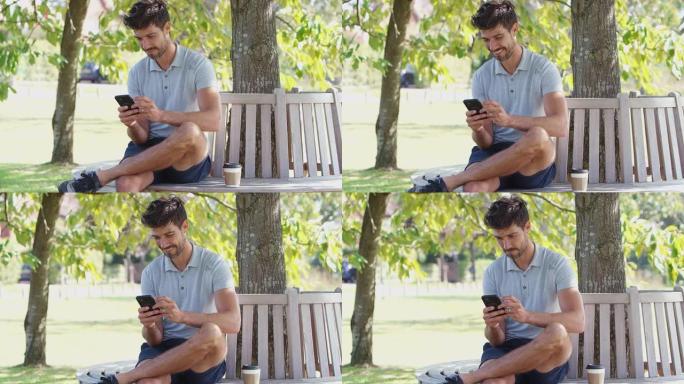男子穿着夏季短裤坐在公园长椅上树下用手机