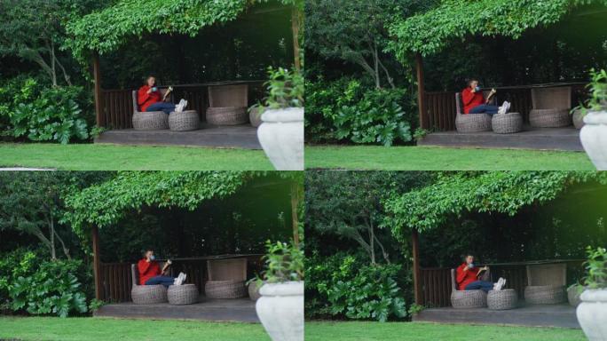 高年级白人妇女在花园里放松，双脚坐着，喝咖啡和看书