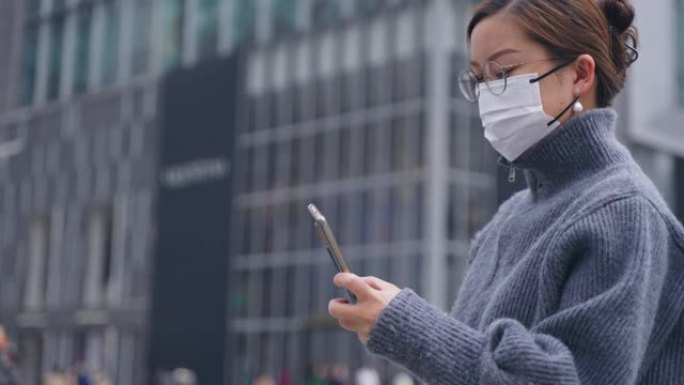 亚洲妇女戴口罩使用电话在城市里行走