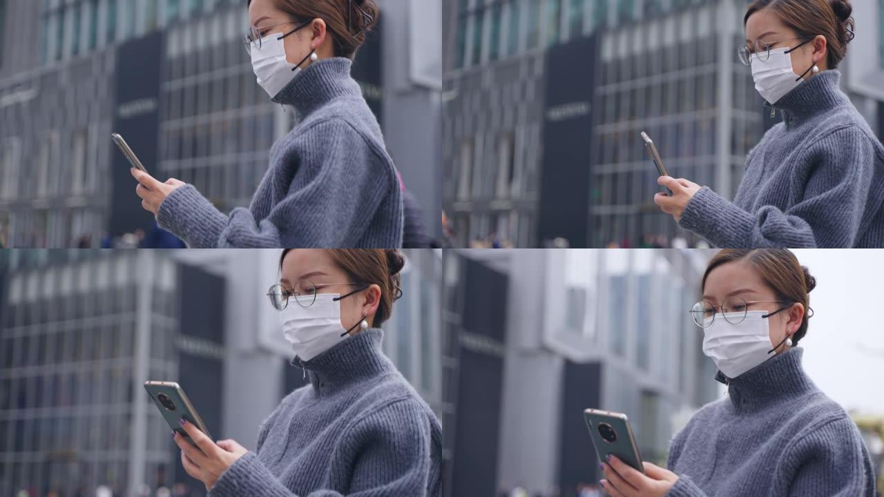 亚洲妇女戴口罩使用电话在城市里行走