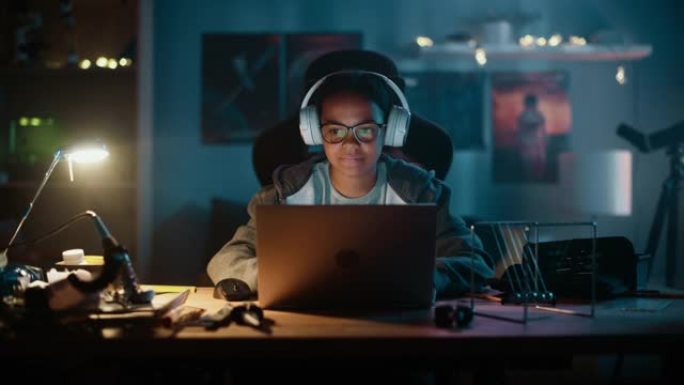 年轻的多种族女孩在家里黑暗舒适的房间里使用笔记本电脑，戴着耳机。她正在网上浏览教育研究。学习科学学校