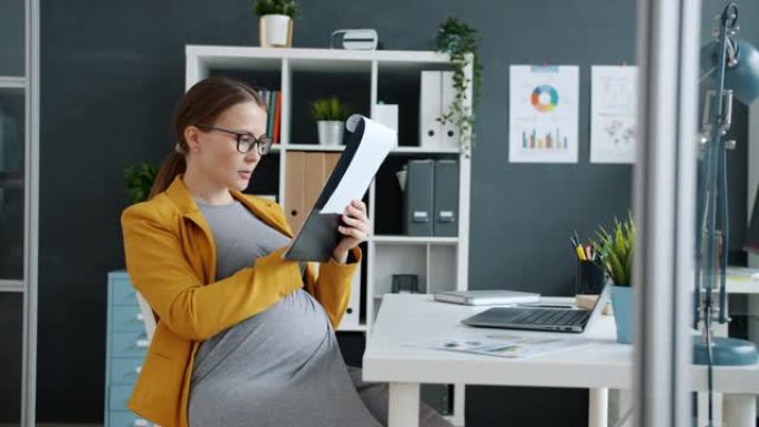 年轻的怀孕女商人在办公室工作，独自坐在办公桌前阅读文件