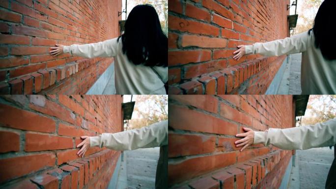 女人走路和手扶着老红砖墙