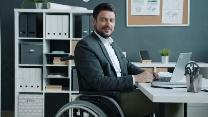 残疾员工坐在轮椅上看着相机并在工作场所微笑的肖像