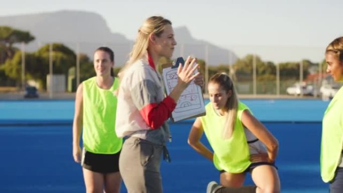 女子曲棍球教练与球员交谈策略，并在练习中激励他们的同时给他们建议。在运动场外训练期间，与体育老师一起
