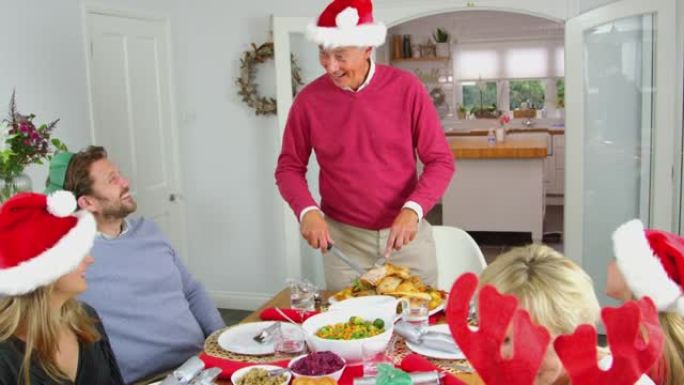 祖父雕刻火鸡作为多代家庭坐下来一起吃圣诞大餐