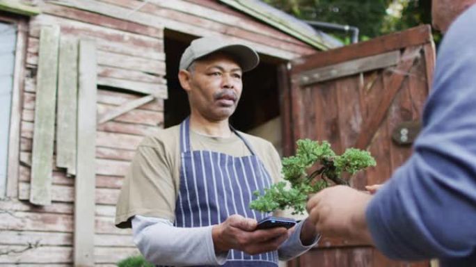 非裔美国男性园丁在花园中心使用非接触式付款来出售植物