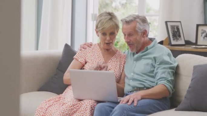 高级退休夫妇坐在家里的沙发上购物或用笔记本电脑预订假期