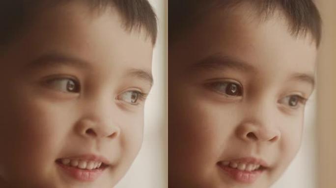 垂直屏幕: 一个可爱的亚洲小男孩转向镜头微笑的肖像。开朗的男孩子站在他家窗户附近。充满天真和惊奇的眼