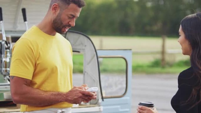 女性客户使用手机向移动咖啡货车的女性所有者进行非接触式付款-慢动作拍摄