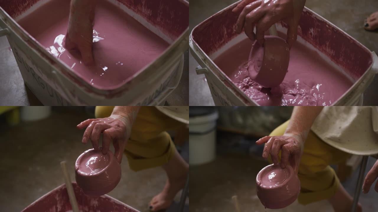 在陶器工作室，女陶工将锅浸入油漆中的特写视图