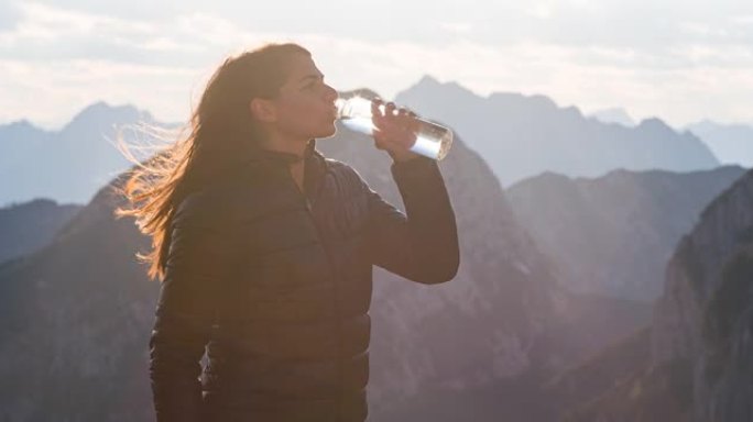 女徒步旅行者在美丽的晴天欣赏山景，喝水