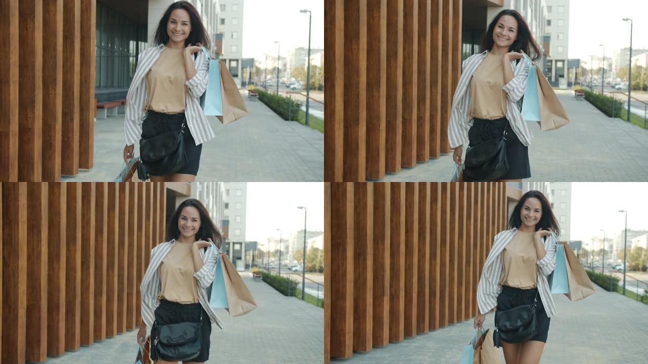 多莉拍摄的迷人的年轻女士带着微笑的购物袋走在户外