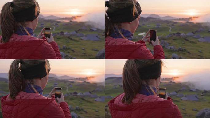 年轻女子用手机拍摄日落的后视图