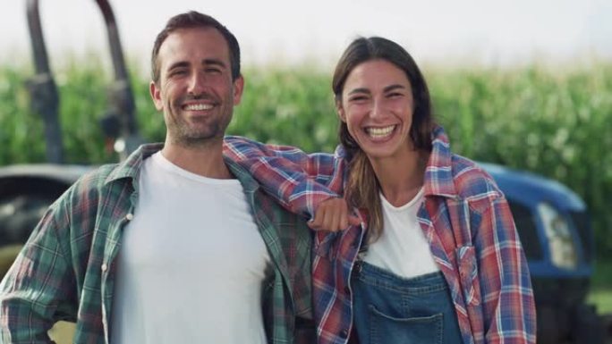 一对幸福的夫妇在满是玉米作物的绿色田野里的拖拉机前摆姿势的肖像。男女农民看着镜头，在农村享受职业和生