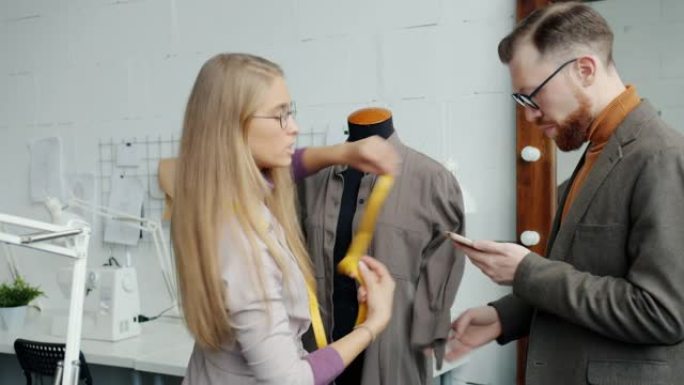 裁缝男女在假人上测量服装，并在工作室室内使用智能手机