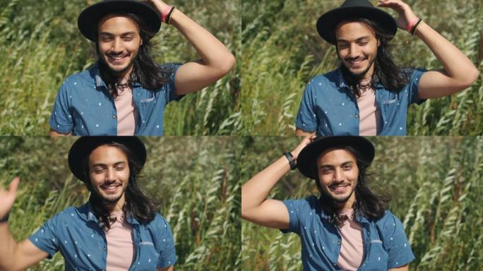 在绿色草地上，英俊的中东家伙在户外触摸帽子和微笑的慢动作肖像