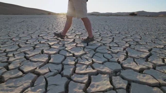 气候变化。由于气候变化和全球变暖造成的干旱，满目疮痍的农民走过干旱大坝的图案化的碎裂泥浆表面的慢动作