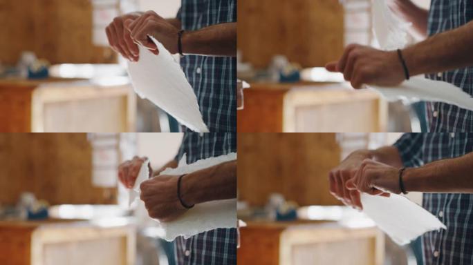 一位工匠造纸大师的特写镜头正在撕下一张手工纸，以控制车间的质量。手工制作的概念，高品质，工匠，意大利
