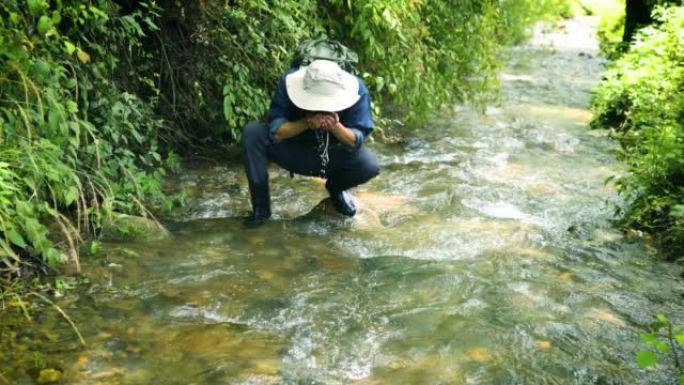 男性徒步旅行者喝溪流中的水