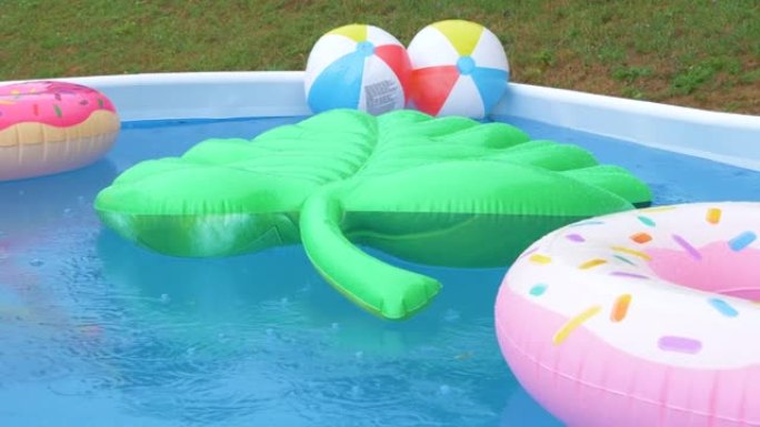 特写: 暴雨期间，充气叶子，甜甜圈和球漂浮在游泳池周围