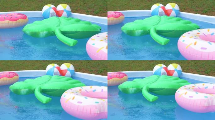 特写: 暴雨期间，充气叶子，甜甜圈和球漂浮在游泳池周围