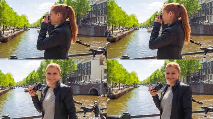 女人享受阳光明媚的日子，欣赏阿姆斯特丹的运河，用老式复古模拟相机拍照，微笑着对着相机